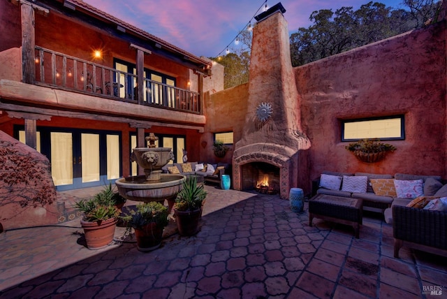 patio terrace at dusk featuring a balcony and an outdoor living space with a fireplace