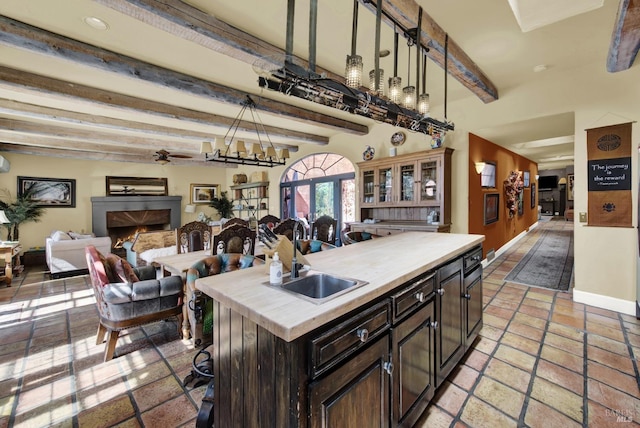 kitchen with hanging light fixtures, a kitchen island with sink, ceiling fan, and beamed ceiling