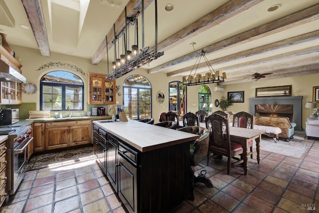 kitchen with ceiling fan, sink, beam ceiling, a kitchen island, and stainless steel range