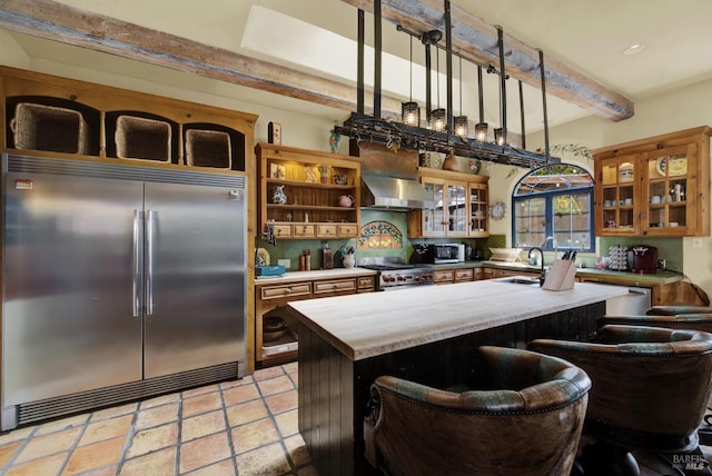 kitchen featuring beamed ceiling, sink, a breakfast bar area, high end appliances, and wall chimney exhaust hood