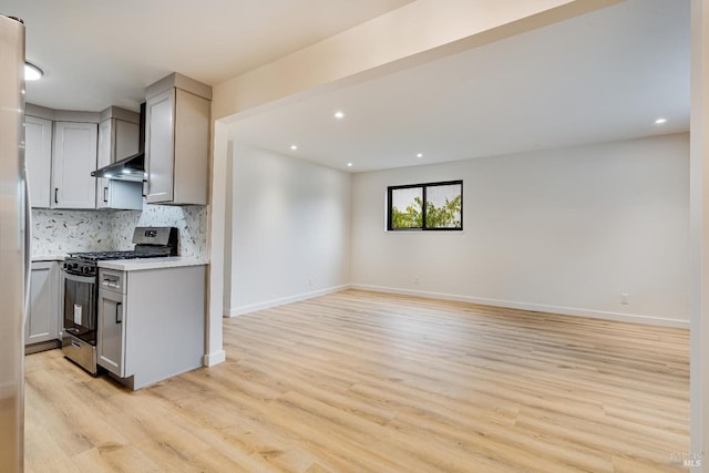 kitchen featuring gray cabinetry, backsplash, wall chimney exhaust hood, light wood-type flooring, and gas stove