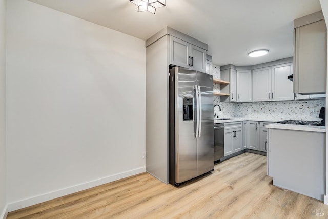 kitchen featuring light countertops, stainless steel appliances, gray cabinetry, backsplash, and a sink