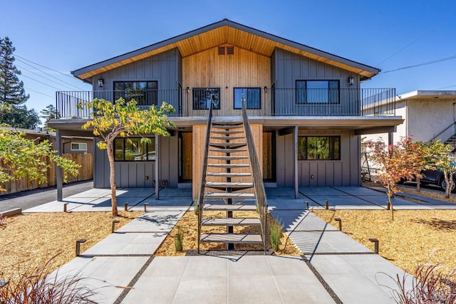 view of front of house featuring stairs, fence, board and batten siding, a balcony, and a patio