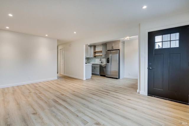 unfurnished living room with light wood-style flooring, a sink, baseboards, and recessed lighting