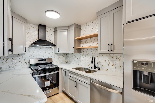 kitchen featuring light stone countertops, sink, stainless steel appliances, and wall chimney range hood