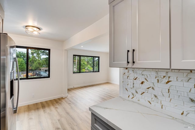 kitchen with stainless steel fridge, light stone countertops, light hardwood / wood-style flooring, and tasteful backsplash