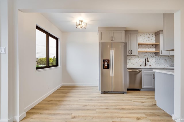 kitchen featuring light countertops, light wood finished floors, tasteful backsplash, appliances with stainless steel finishes, and gray cabinetry