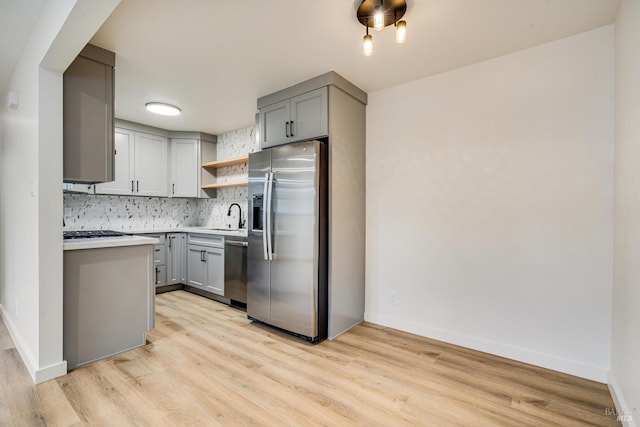 kitchen with open shelves, gray cabinetry, backsplash, a sink, and appliances with stainless steel finishes