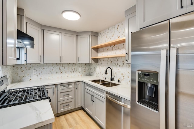 kitchen featuring decorative backsplash, light stone counters, stainless steel appliances, sink, and light hardwood / wood-style flooring