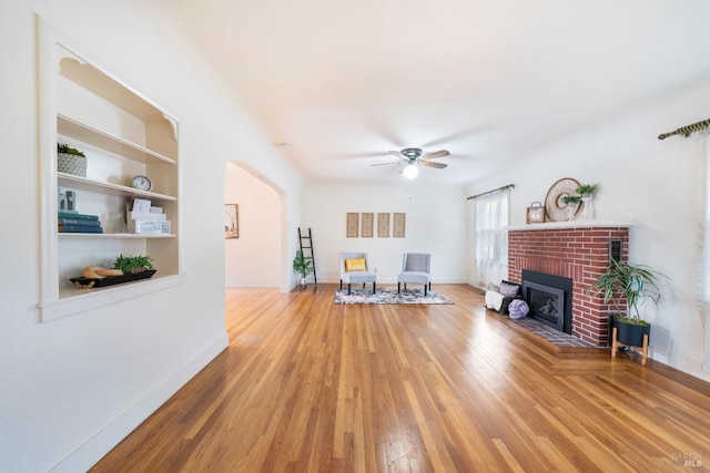 living room featuring hardwood / wood-style flooring, ceiling fan, built in features, and a brick fireplace