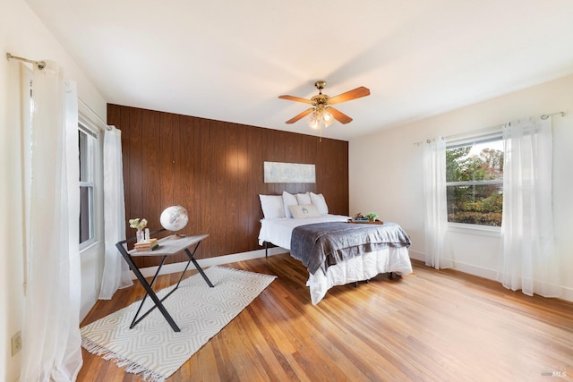 bedroom with ceiling fan, wooden walls, and light hardwood / wood-style floors