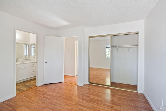 unfurnished bedroom featuring a closet, a textured ceiling, sink, light hardwood / wood-style flooring, and ensuite bath