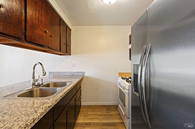 kitchen featuring dark brown cabinetry, sink, light hardwood / wood-style flooring, stainless steel refrigerator with ice dispenser, and white range with gas cooktop