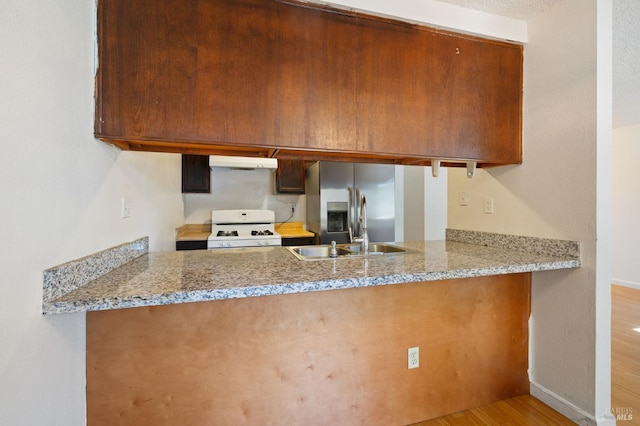 kitchen featuring light stone counters, stainless steel fridge, gas range gas stove, exhaust hood, and hardwood / wood-style floors