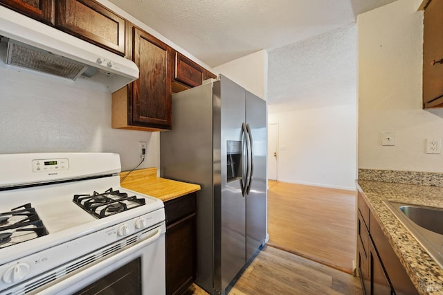 kitchen featuring light stone counters, a textured ceiling, light hardwood / wood-style floors, stainless steel fridge with ice dispenser, and white range with gas cooktop