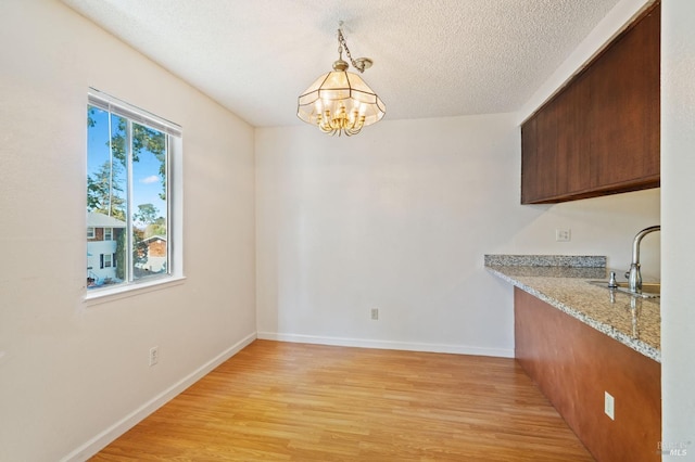 unfurnished dining area with a notable chandelier, a textured ceiling, light hardwood / wood-style floors, and sink