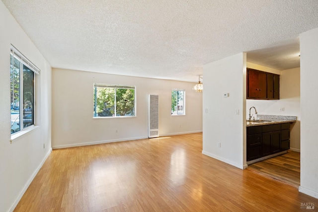 unfurnished living room with an inviting chandelier, a textured ceiling, light hardwood / wood-style floors, and sink