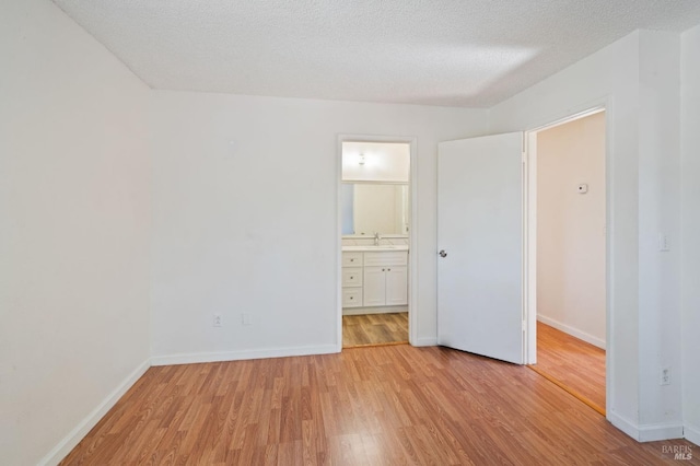 unfurnished bedroom with a textured ceiling, light wood-type flooring, ensuite bath, and sink