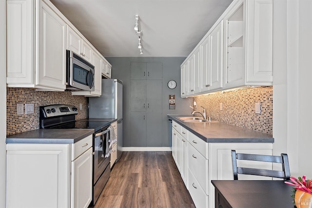 kitchen featuring dark countertops, a sink, white cabinetry, dark wood finished floors, and appliances with stainless steel finishes
