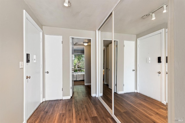 hall with baseboards, track lighting, and wood finished floors