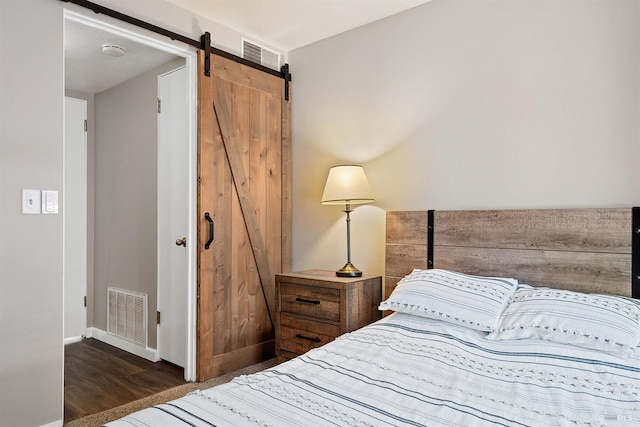 bedroom featuring a barn door, baseboards, wood finished floors, and visible vents