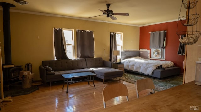 bedroom with ceiling fan, multiple windows, hardwood / wood-style floors, and a wood stove