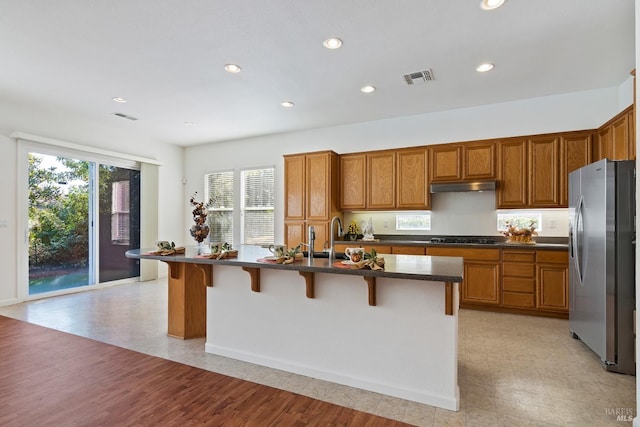 kitchen featuring stainless steel fridge, black gas cooktop, a kitchen island with sink, a breakfast bar area, and light wood-type flooring