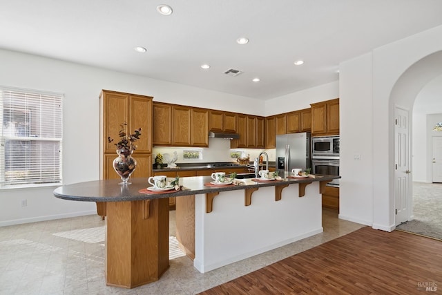 kitchen with a kitchen bar, a center island with sink, and appliances with stainless steel finishes