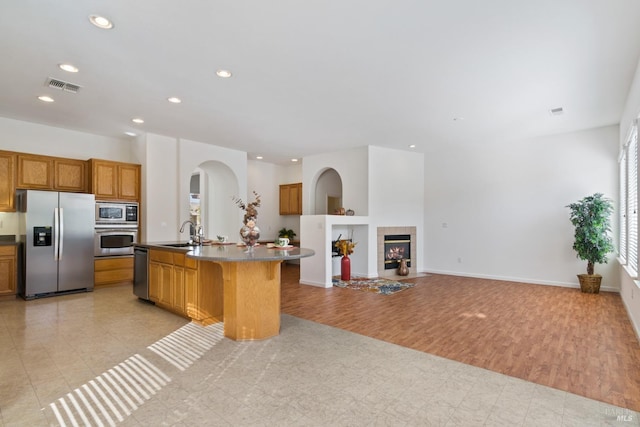 kitchen with light hardwood / wood-style floors, an island with sink, a tile fireplace, stainless steel appliances, and sink