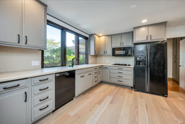 kitchen featuring gray cabinetry, backsplash, black appliances, light hardwood / wood-style flooring, and sink