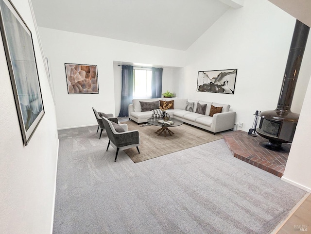 living room featuring high vaulted ceiling, a wood stove, baseboards, and carpet floors