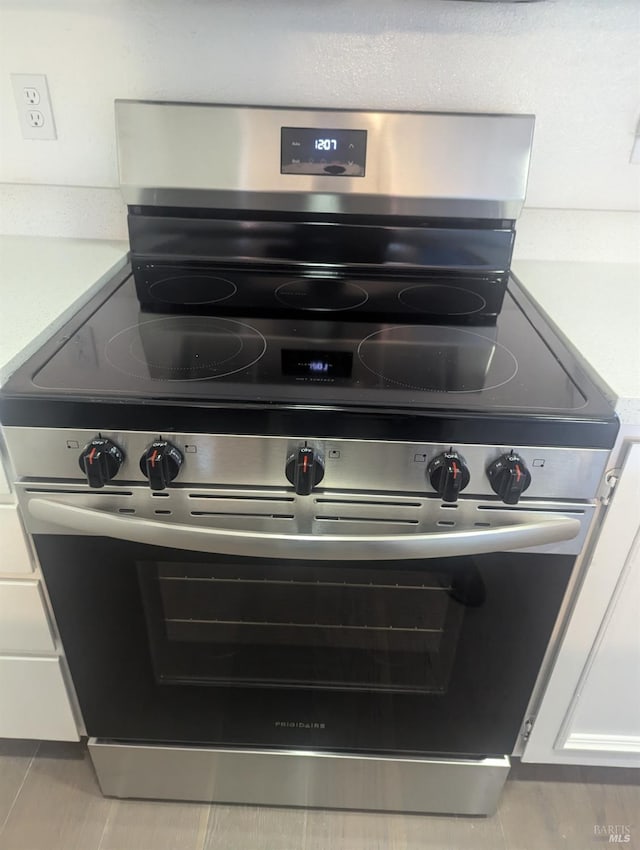 interior details with white cabinets, stainless steel electric range, and light countertops