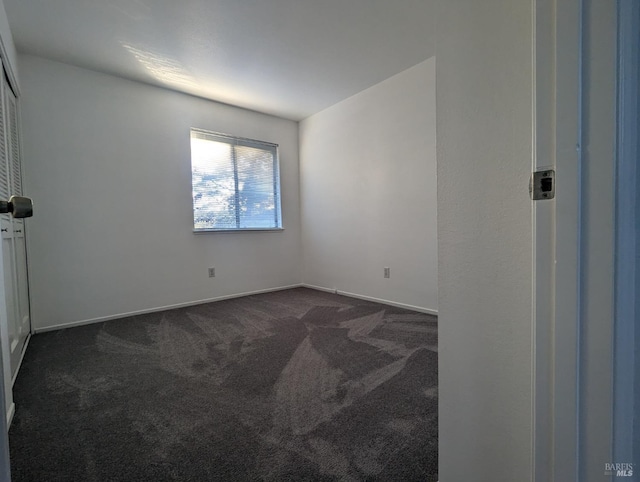 empty room featuring dark carpet and baseboards