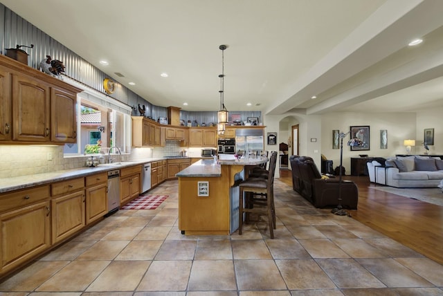 kitchen featuring a breakfast bar, pendant lighting, tasteful backsplash, light stone counters, and a center island with sink