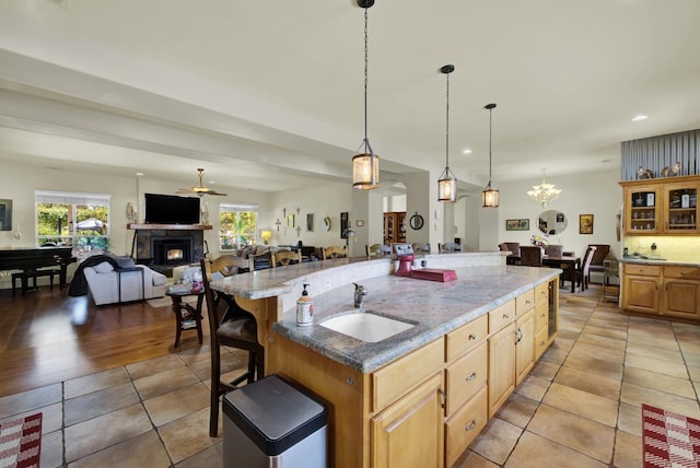 kitchen featuring a spacious island, sink, hanging light fixtures, a kitchen breakfast bar, and light stone countertops