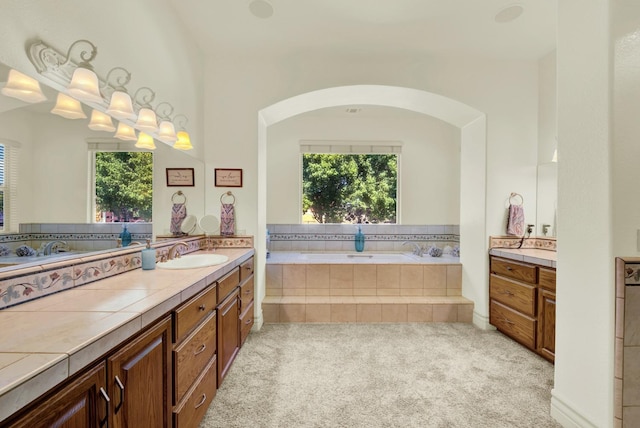 bathroom with vanity, plenty of natural light, and tiled bath