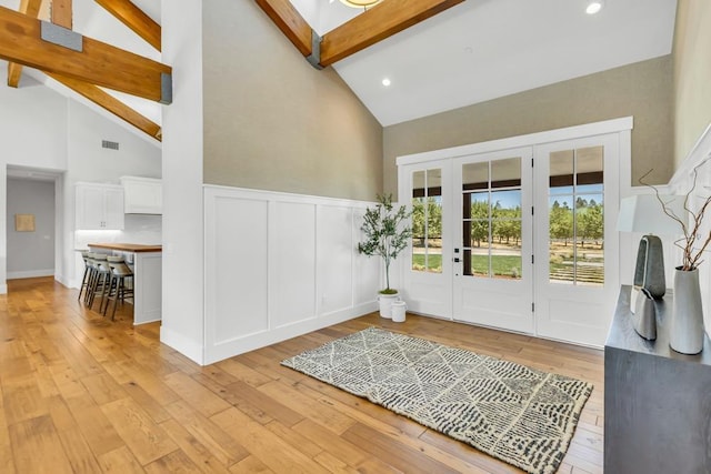 foyer entrance with high vaulted ceiling, light wood-type flooring, and beam ceiling