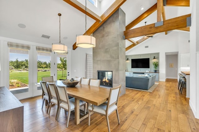 dining space featuring beam ceiling, high vaulted ceiling, a fireplace, and light wood-type flooring