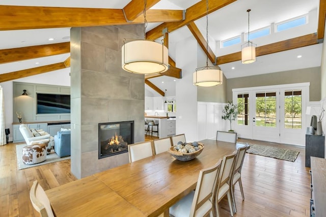 dining space featuring a tile fireplace, high vaulted ceiling, light wood-type flooring, and beam ceiling