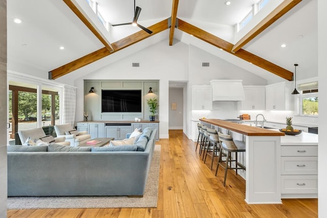 living room with beamed ceiling, high vaulted ceiling, sink, and light hardwood / wood-style floors