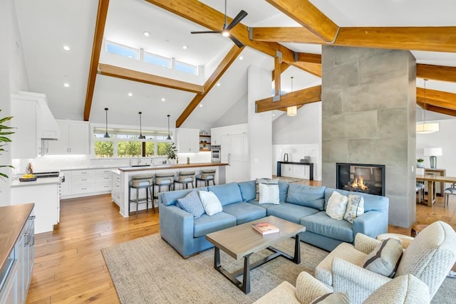 living room with a tile fireplace, high vaulted ceiling, ceiling fan, light hardwood / wood-style floors, and beam ceiling