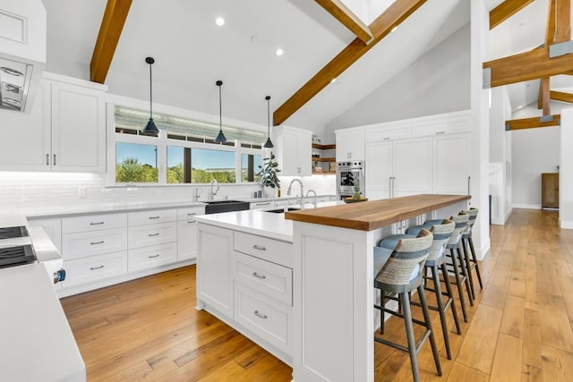 kitchen featuring a kitchen island, beamed ceiling, white cabinetry, butcher block counters, and hanging light fixtures