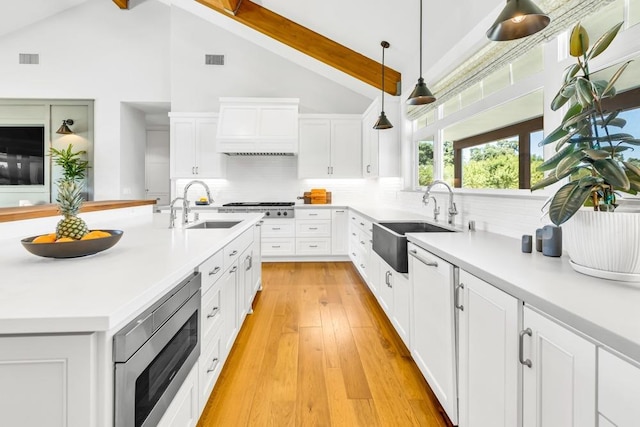 kitchen featuring pendant lighting, white cabinetry, sink, stainless steel appliances, and custom range hood