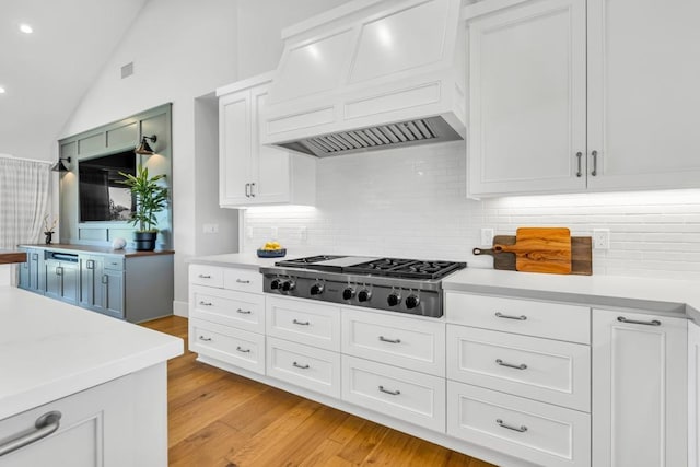 kitchen featuring custom exhaust hood, lofted ceiling, white cabinets, and stainless steel gas stovetop