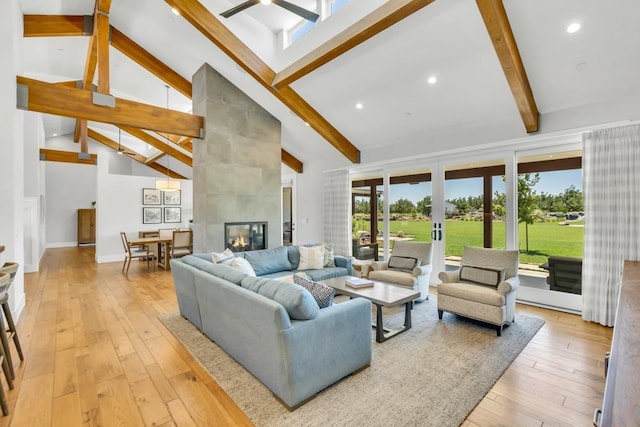 living room featuring high vaulted ceiling, a tile fireplace, light hardwood / wood-style floors, and beamed ceiling