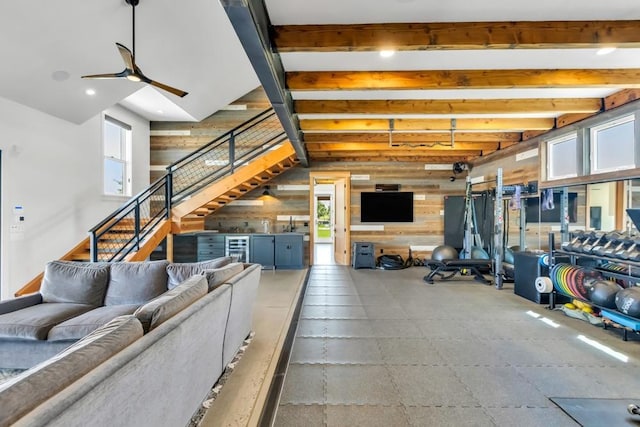 living room featuring beamed ceiling, wooden walls, stairway, and a ceiling fan