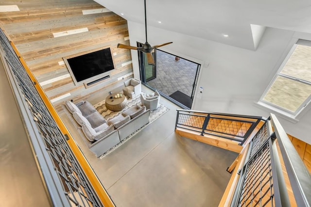 living room featuring wooden walls, concrete floors, and ceiling fan