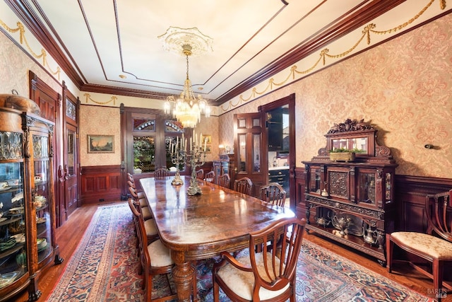 dining area with wood-type flooring, an inviting chandelier, and ornamental molding