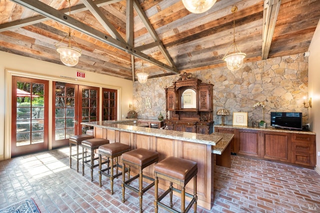 kitchen featuring light stone counters, beam ceiling, hanging light fixtures, high vaulted ceiling, and a kitchen breakfast bar