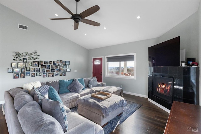 living area featuring dark wood-style flooring, visible vents, a glass covered fireplace, vaulted ceiling, and baseboards